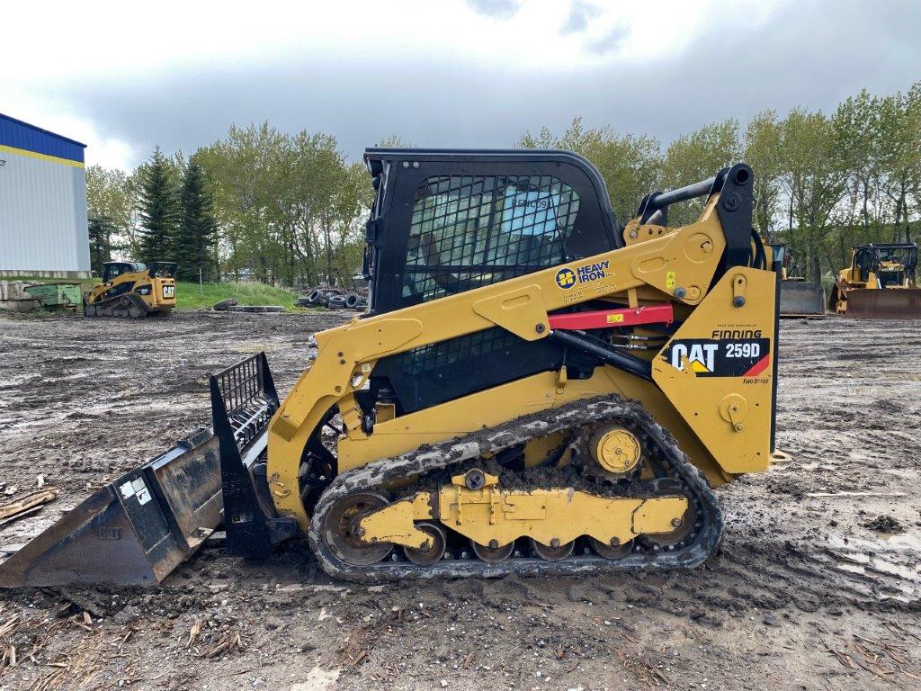 CAT 259D compact track loader with front bucket at a Heavy Iron Inc. equipment yard.